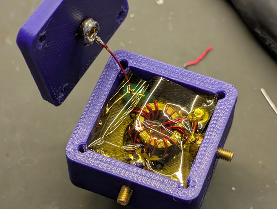 The internals of the unun with kapton tape covering the torroid, and the 49:1 antenna connection brass screw in the lid at the upper left.