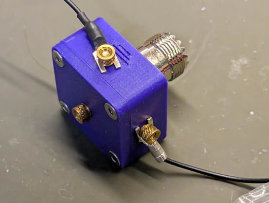The assembled unun with two wires attached. At the top is a wire next to a ground symbol on the side of the 3d-printed box. This wire is the counterpoise. On the lower right is another wire connected to the side of the box. This is the random wire connected to the 9:1 antenna connection. At the lower left, in the middle of the lid, is the antenna connection for an end-fed half-wave antenna.

Each of the terminals uses a heat-set insert as a finger nut to connect the antennas.