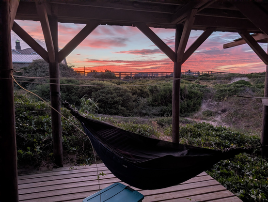 Hammock slung under an elevated beach house, tied to pilings, with a beautiful sunrise in the background. It was a great way to wake up!