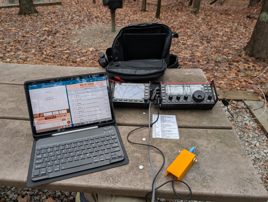 Picnic table set up for POTA with KX3, PA2, my own single-paddle key, and a tablet on a stand with a keyboard.