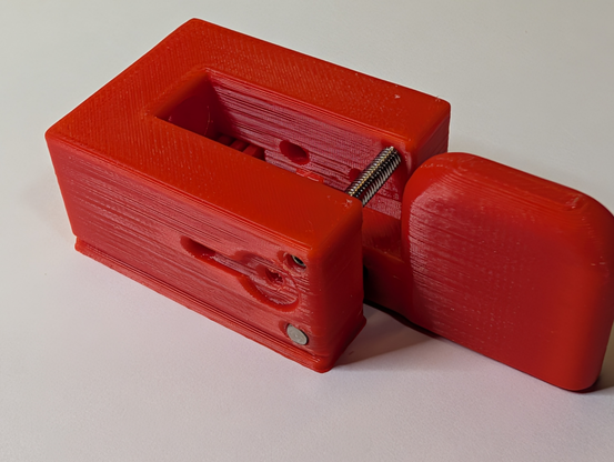 Photo of a red single-paddle morse code key with a screw installed. The screw holds the arms apart to make them more rigid.
The key has not been fully assembled; most of the hardware is still missing. This photo is from the assembly instructions.