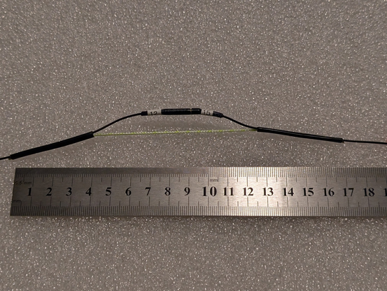 Photo of an antenna link between 12 meter and 15 meter segments, shown above a metric scale. The entire link is between 17 and 18 cm long. Dacron cord carries the load between the two segments, which are connected by banana plugs insulated by more heat shrink.