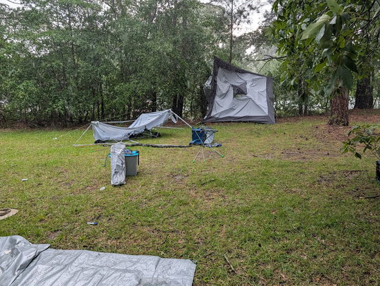 Photo showing one pop-up shelter plastered against trees and bushes, and another destroyed.