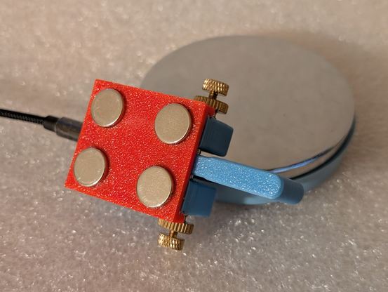 Photo of the underside of a magnet mount holding a Morse key, next to a jeweler's block